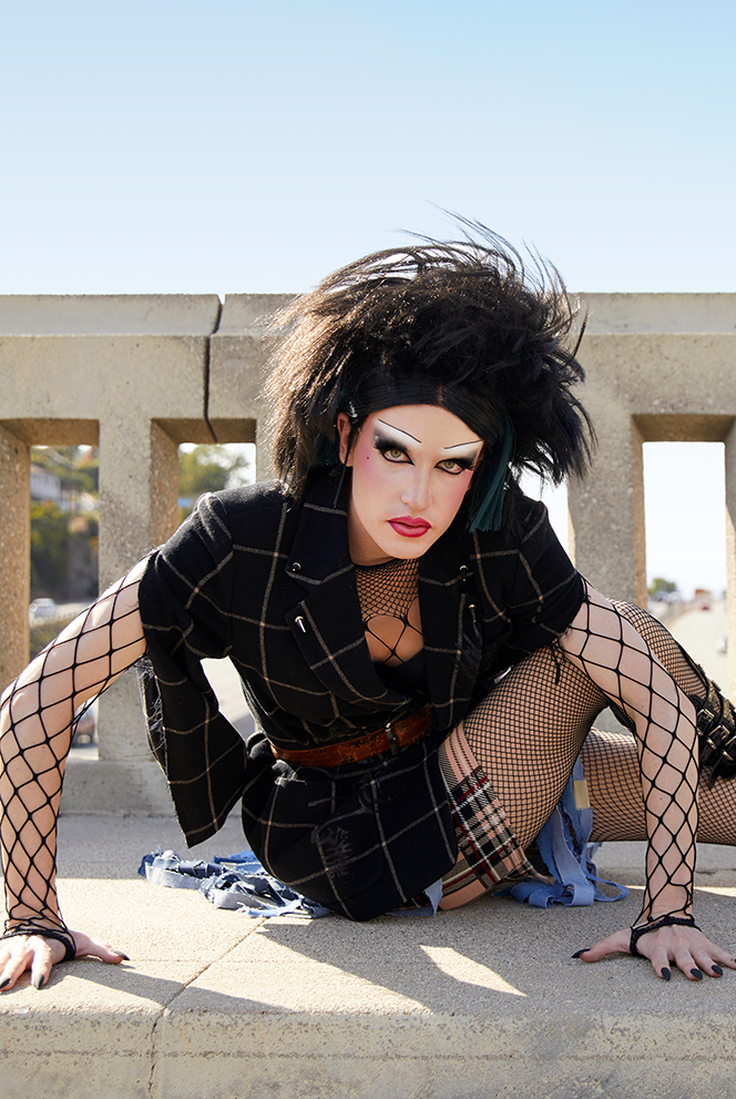 Close up portriat of Jesse in Punk drag sitting on the ground and leaning in towards the camera.